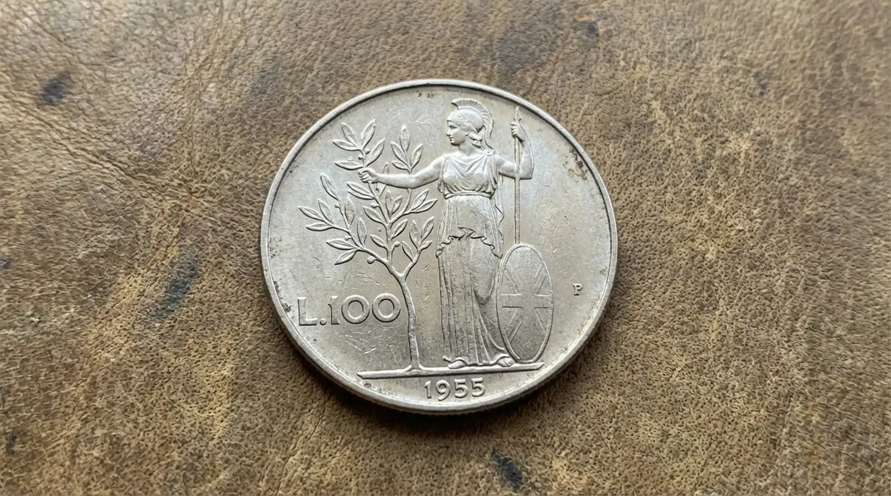 Moneta da 100 lire Minerva del 1955, con figura di Minerva e albero d’ulivo, fotografata su superficie marrone