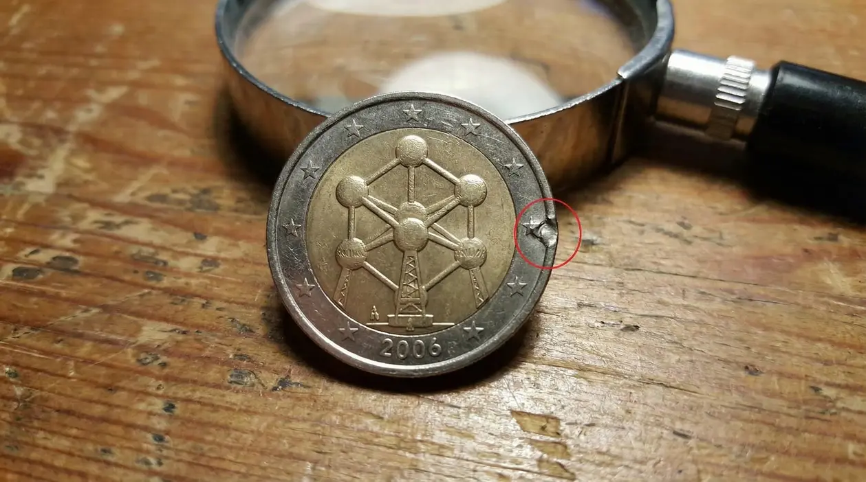 Moneta da 2 euro Belgio 2006 con difetto sul bordo, vicino a una lente d’ingrandimento