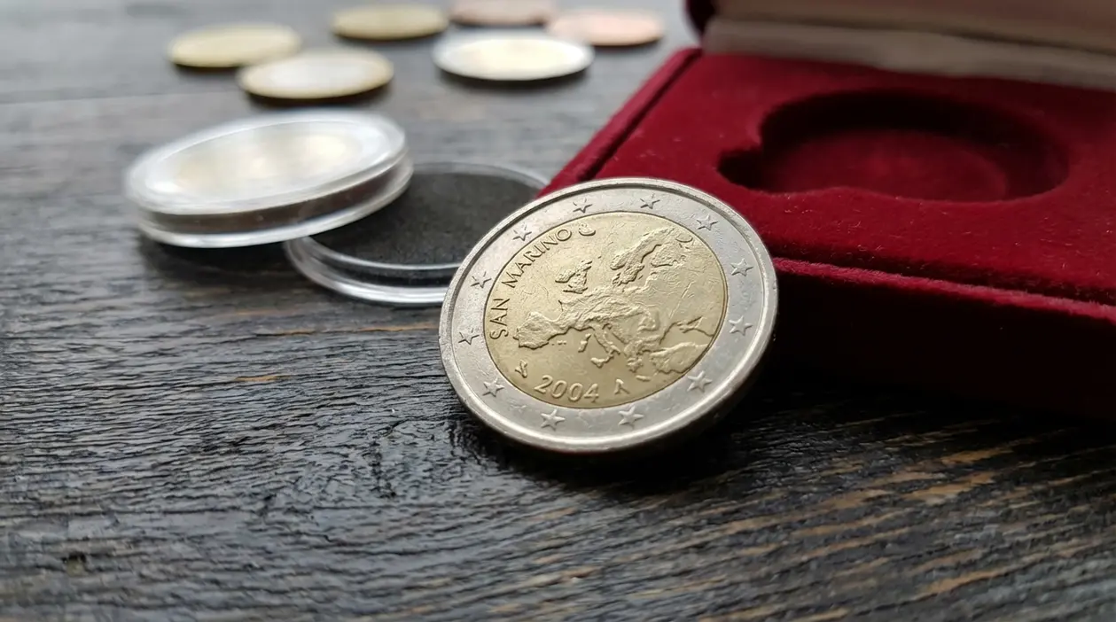 Moneta da 2 euro di San Marino del 2004 su tavolo, accanto a capsule trasparenti e custodia in velluto rosso