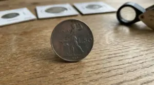 Moneta italiana da 50 lire Vulcano del 1958 su tavolo in legno, con lente d’ingrandimento sullo sfondo