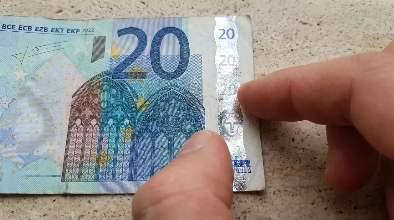 Dettaglio di una banconota da 20 euro con dito che indica la banda olografica, usata per verificare l’autenticità