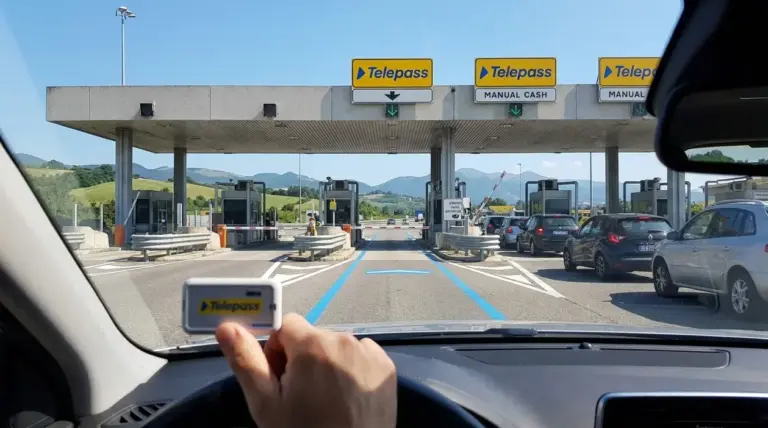 Casello autostradale con corsie per telepedaggio e auto in coda, visto dall’interno di un’auto