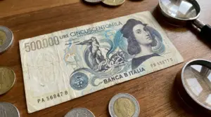 Banconota italiana da 500.000 lire su tavolo in legno con monete e lente d’ingrandimento