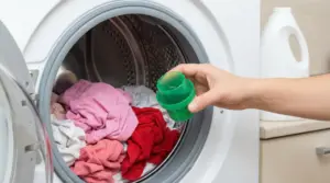 Una mano tiene un dosatore davanti a una lavatrice carica di panni colorati