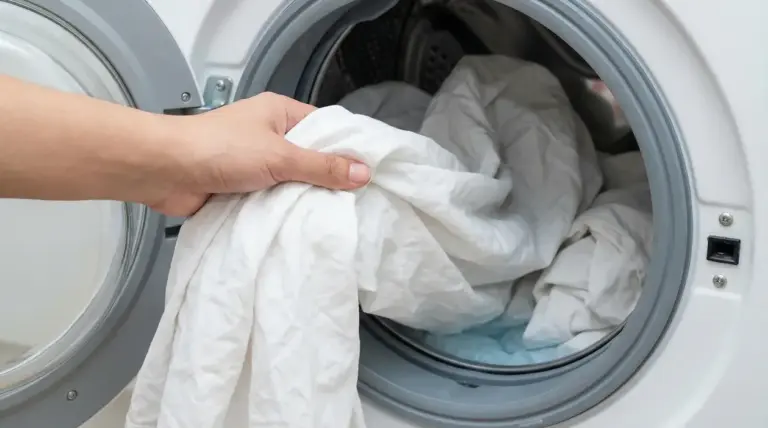 Una mano inserisce lenzuola bianche in una lavatrice aperta
