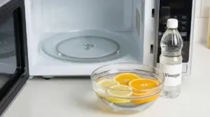 Ciotola con fette di agrumi in acqua accanto a una bottiglia di aceto e un forno a microonde aperto