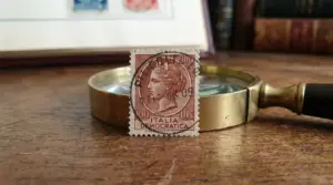Francobollo Italia “Democratica” da 100 lire (1948) con annullo, appoggiato a una lente d’ingrandimento su un tavolo