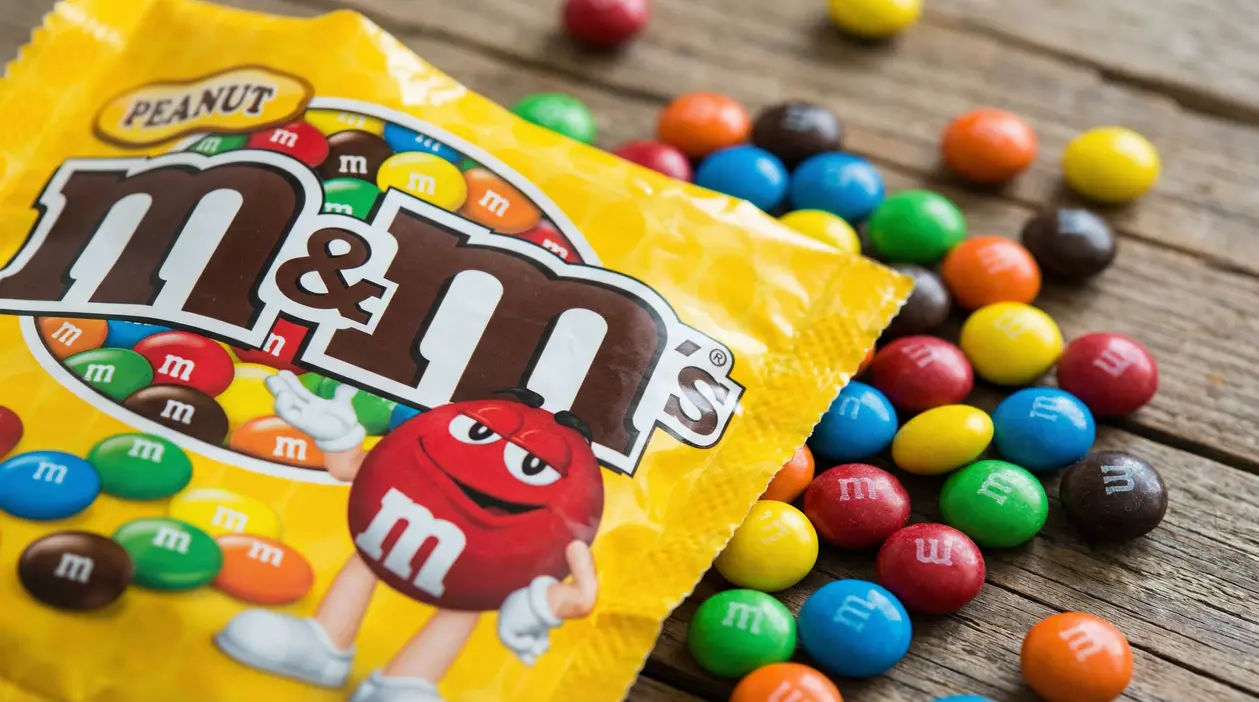 Confezione gialla di M&M's Peanut con confetti colorati sparsi su una superficie di legno
