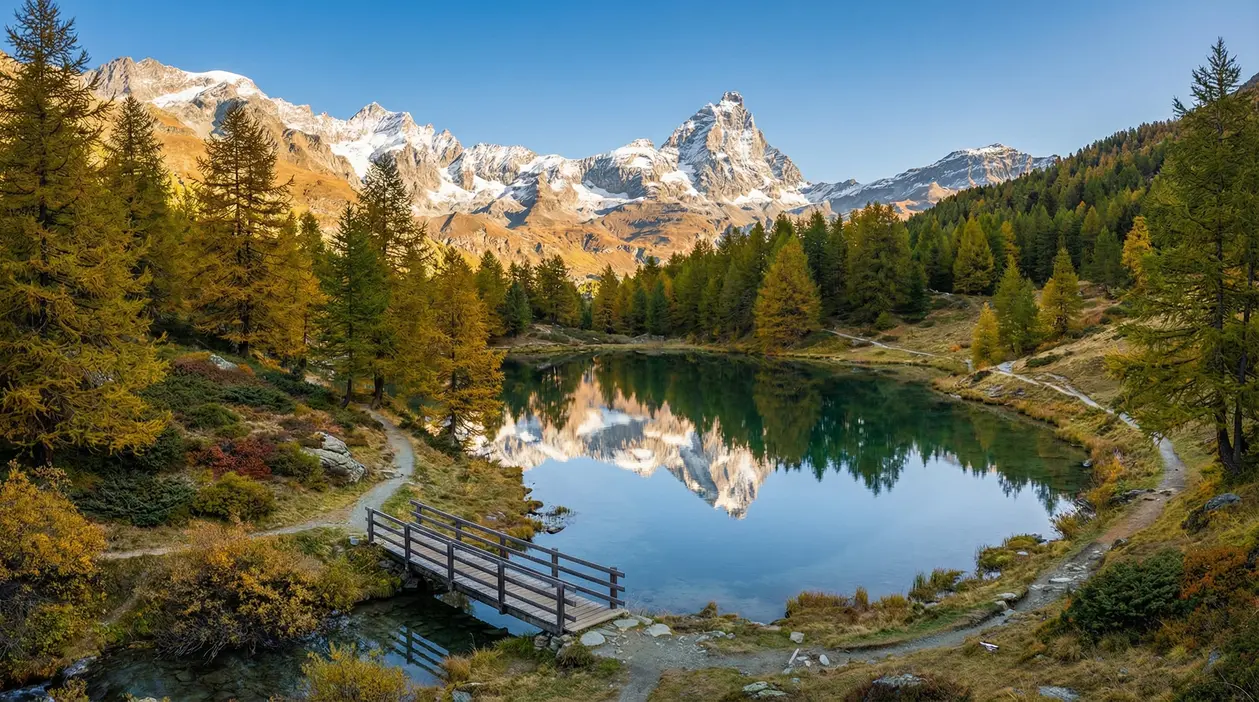 Lago alpino circondato da alberi autunnali e montagne innevate in Valle d'Aosta