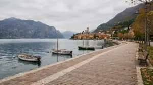Passeggiata autunnale sul lungolago di Garda con barche ormeggiate e le montagne sullo sfondo