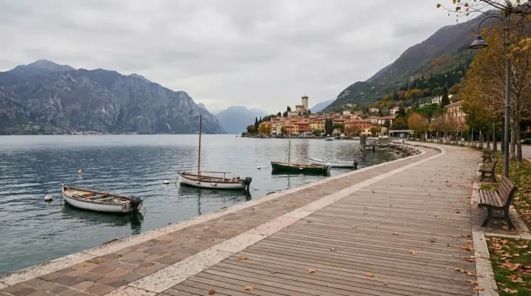 Passeggiata autunnale sul lungolago di Garda con barche ormeggiate e le montagne sullo sfondo