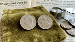 Moneta italiana da 10 lire del 1960 fotografata su panno, con lente d’ingrandimento e altre monete sullo sfondo