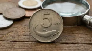Moneta da 5 lire con delfino del 1956 in primo piano su tavolo di legno
