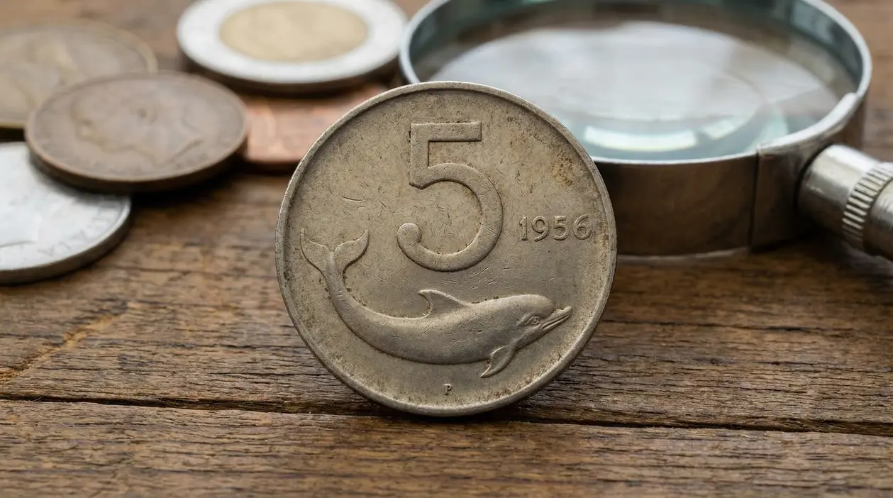 Moneta da 5 lire con delfino del 1956 in primo piano su tavolo di legno