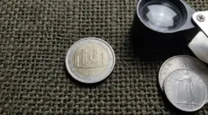 Moneta da 2 euro italiana del 2018 su tessuto, accanto a lente d’ingrandimento per controllare un microerrore