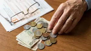 Mano di una persona che conta monete e banconote accanto a documenti e occhiali su un tavolo