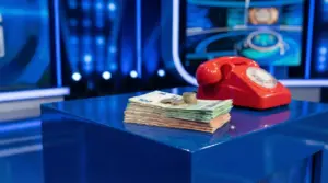 Mazzo di banconote e monete vicino a un telefono rosso su un tavolo blu in uno studio televisivo