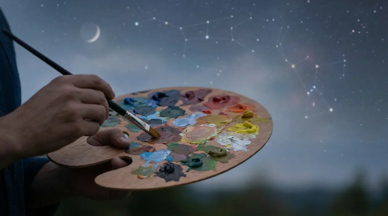 Mano che tiene una tavolozza piena di colori con sfondo di cielo stellato e costellazioni