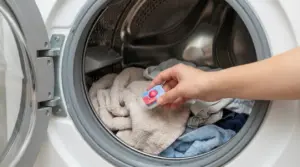 Mano che inserisce una pastiglia per lavastoviglie all'interno di una lavatrice piena di panni