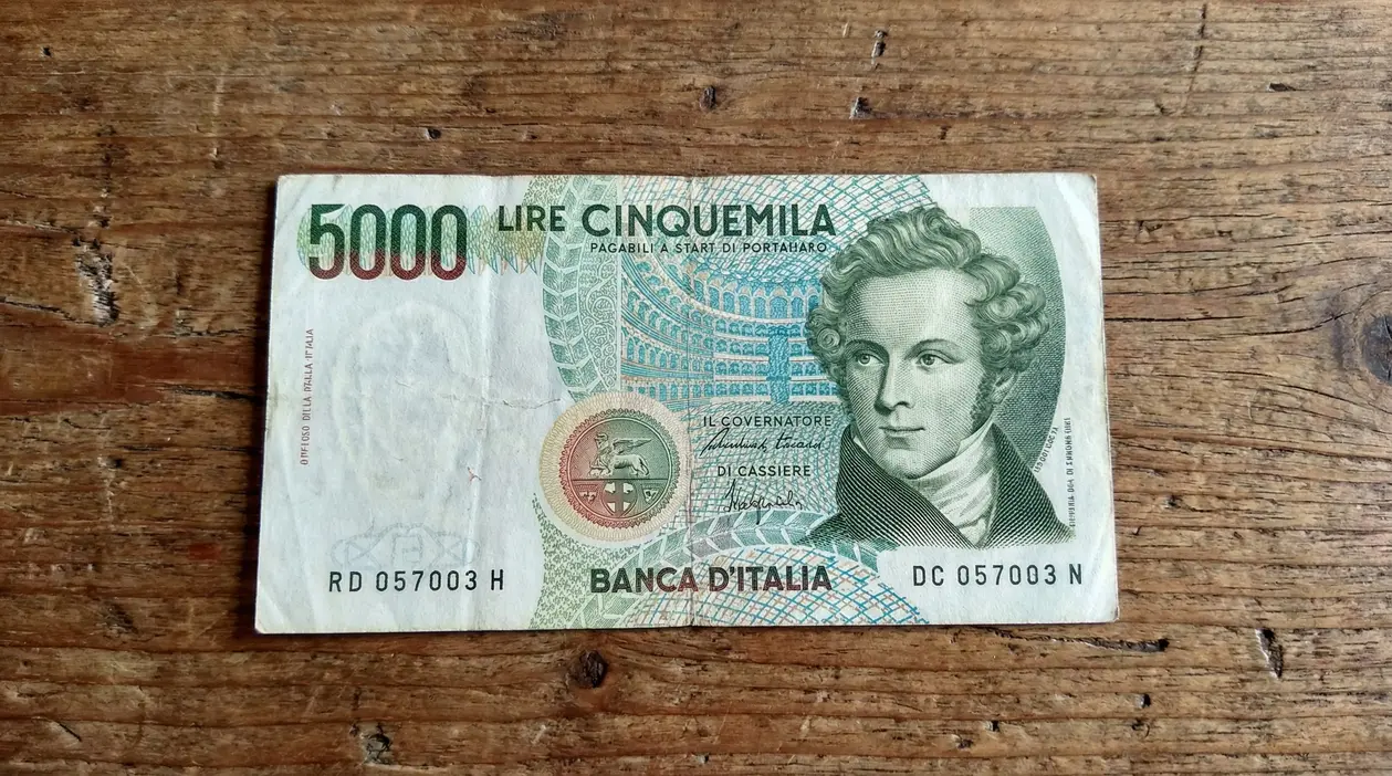 Vecchia banconota da 5.000 lire italiane appoggiata su un tavolo di legno