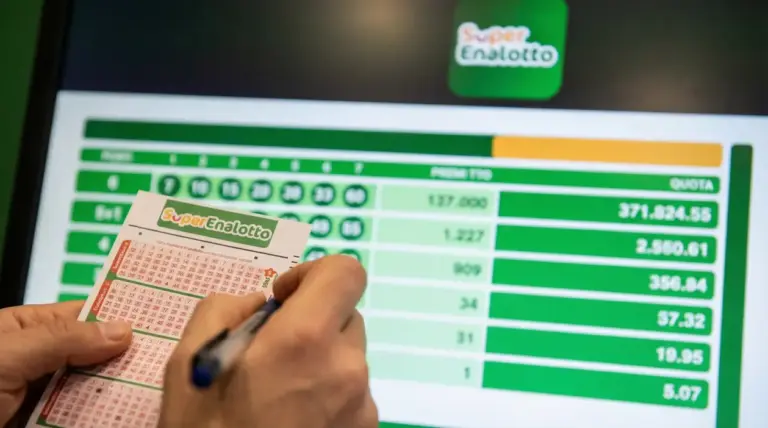 Mani che compilano una schedina del SuperEnalotto davanti a uno schermo con tabella di quote e premi