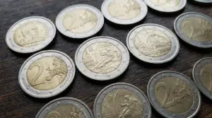 Monete da 2 euro, incluse versioni commemorative, disposte su un tavolo in legno